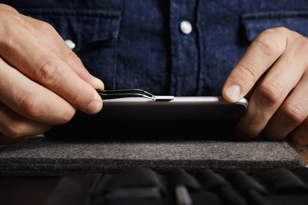 Бесплатное фото Угловой пинцет для эсд, вытаскивающий лоток для микро-сим-карты из корпуса мобильного смартфона рядом с сумкой с инструментами