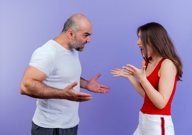 Angry adult couple standing in profile view both spreading hands and arguing with each other 