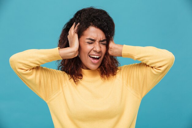 Angry african woman in sweater screaming and covering her ears