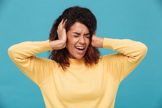 Angry african woman in sweater screaming and covering her ears