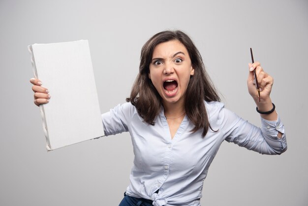 Angry artist with empty canvas screaming on gray wall. 