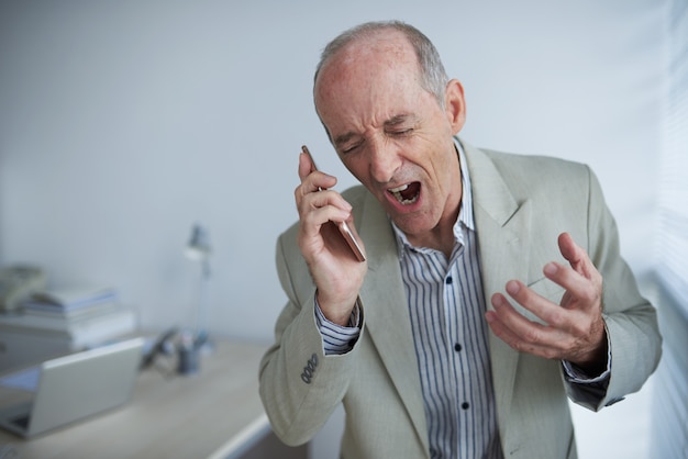 Angry bald Caucasian businessman holding mobile phone and screaming with rage