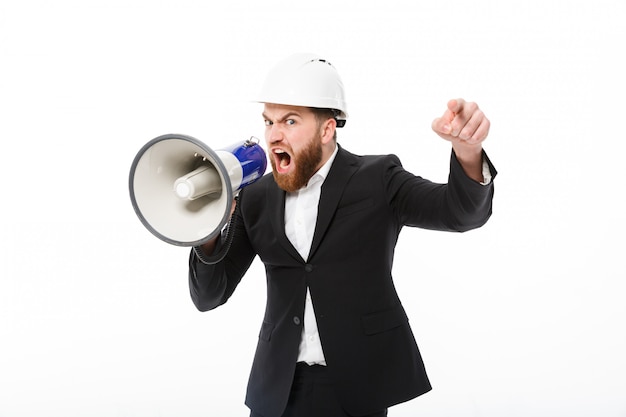 Free photo angry bearded business man in protective helmet screaming in megaphone