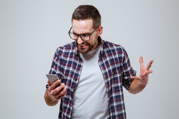 Angry Bearded man in eyeglases looking at phone
