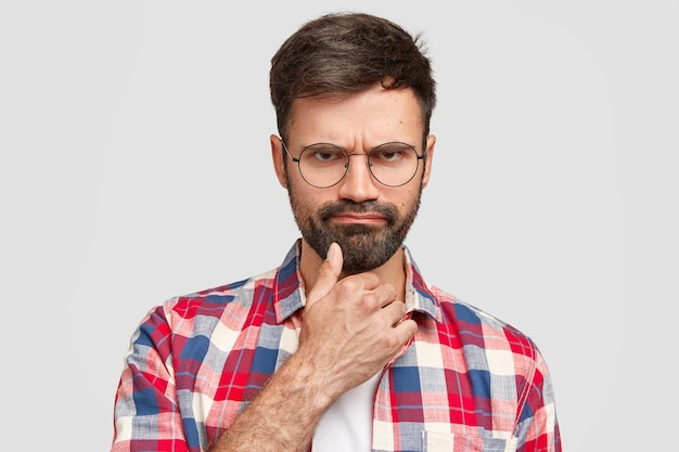 Angry bearded man has sullen expression, looks under eyebrows, being displeased with bad news