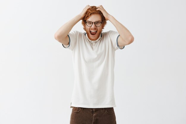 Angry bearded redhead guy posing against the white wall with glasses