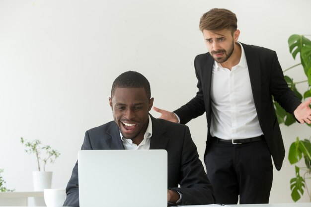 Angry boss catching african employee entertaining online instead of work