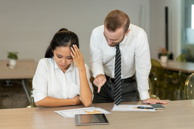 Free photo angry boss pointing at report while berating asian employee