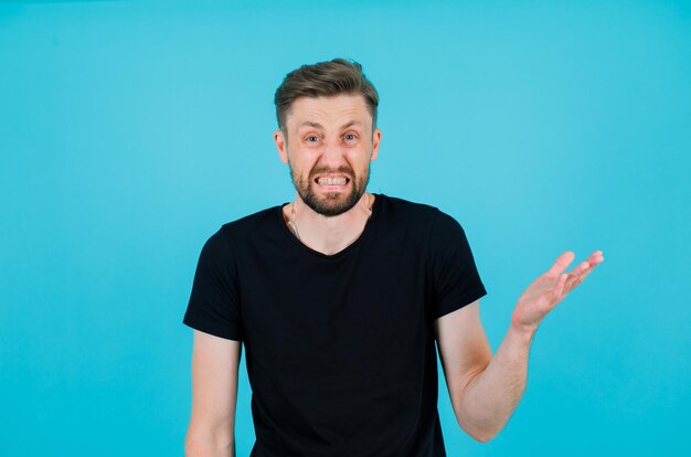 Angry boy is looking at camera by raising up his hand on blue background