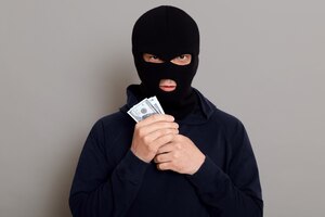 怒った泥棒の男が偽造された表情で正面を見て、盗まれたお金を手に持っている