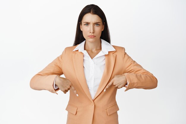 怒っているビジネスの女性が販売バナーを心配して指を下に向けて白い背景に対してスーツに立っているsmthに不平を言う女性起業家