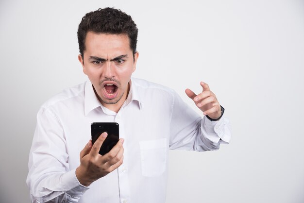 Angry businessman screaming at cellphone on white background.