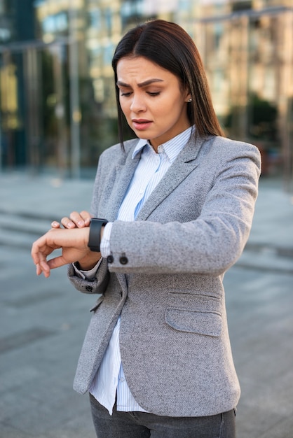 屋外で彼女の時計を見ている怒っている実業家