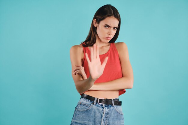 Angry casual girl  sadly looking in camera showing stop gesture over colorful background isolated