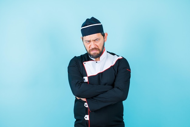 Angry chef is looking at camera by crossing arms on blue background
