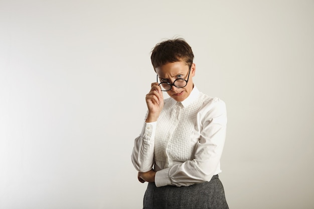 Angry crazy looking teacher adjusting her round black glasses on white wall