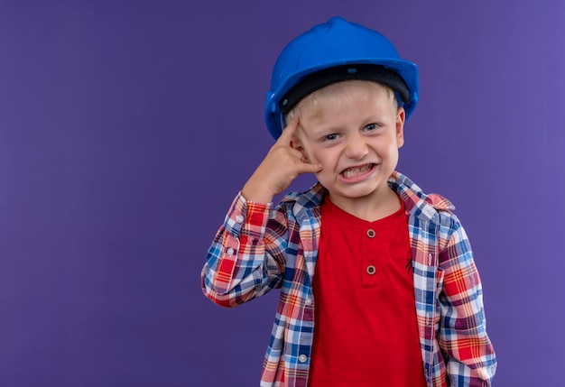 Злой милый маленький мальчик со светлыми волосами в клетчатой рубашке в синем шлеме смотрит