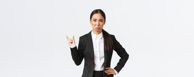 Angry disappointed saleswoman in black suit complaining on small miserable size showing something tiny and pouting displeased standing bothered over white background Copy space