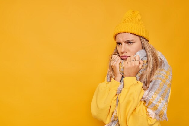 怒った不機嫌な女性は、首の周りに暖かいスカーフを身に着けている不機嫌そうな表情で見え、あなたのプロモーションコンテンツの黄色の背景の空白に対して不幸なポーズを感じます。否定的な感情の概念