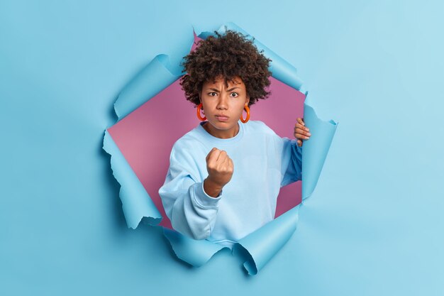 Angry dissatisfied young Afro American woman shows fists and expresses negative emotions