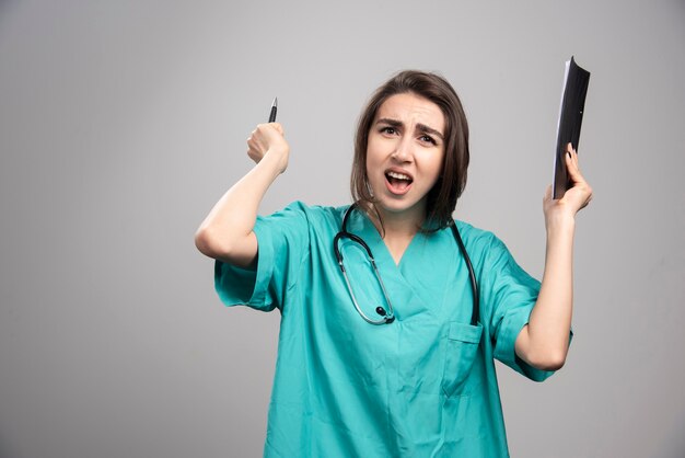 Medico arrabbiato che tiene appunti e penna su sfondo grigio. foto di alta qualità