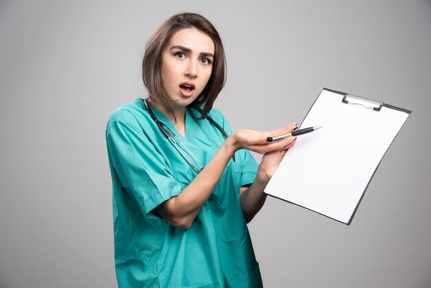 Angry doctor pointing at clipboard on gray background. High quality photo