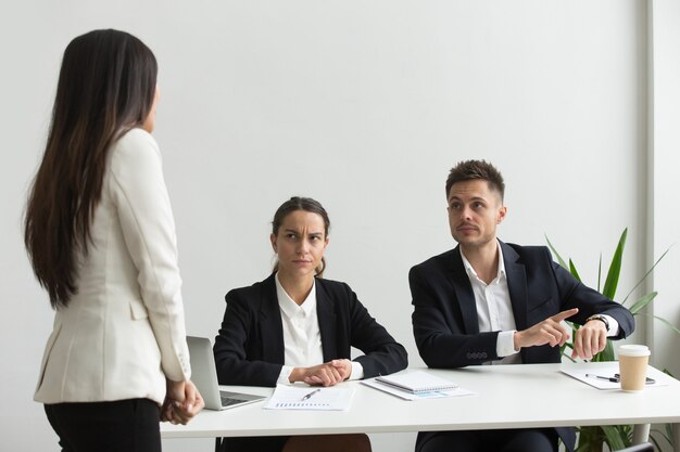 Angry executive pointing at wristwatch scolding employee for being late