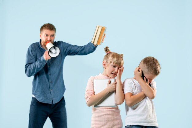 Angry father scolding his son and daughter at home. Studio shot of emotional family. Human emotions, childhood, problems, conflict, domestic life, relationship concept