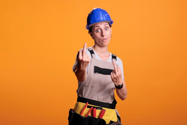 Free photo angry female builder showing middle finger in studio, doing rude gesture and acting aggressive. making disapproving signs and expressing negative emotion, displeased handywoman.