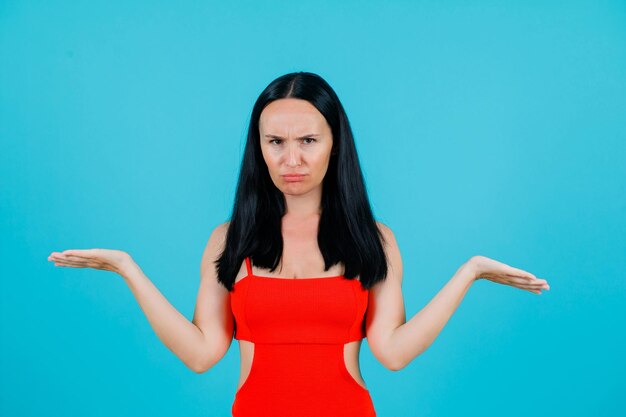 Angry girl is looking at camera by opening wide her arms on blue background