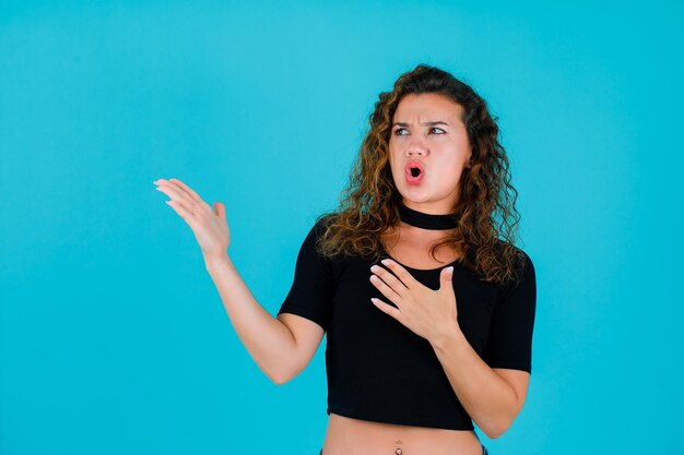 Angry girl is looking left by pointing left with hands on blue background