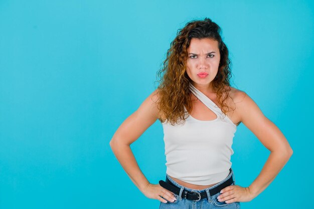 Angry girl is looking up by putting hands on waist on blue background