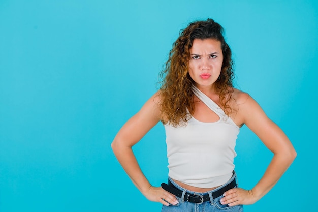 Angry girl is looking up by putting hands on waist on blue background