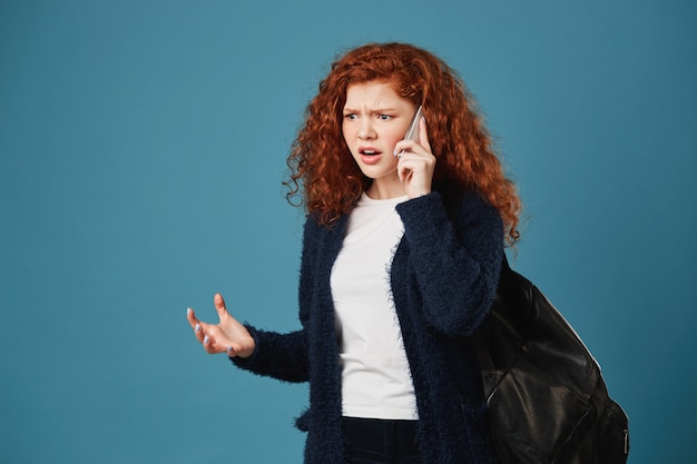 Angry handsome student woman looking aside, expressive gesticulating with hands, arguing with mother about study on phone.