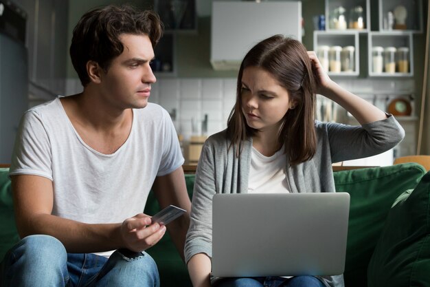 Angry husband holding credit card blaming wife of overspending money