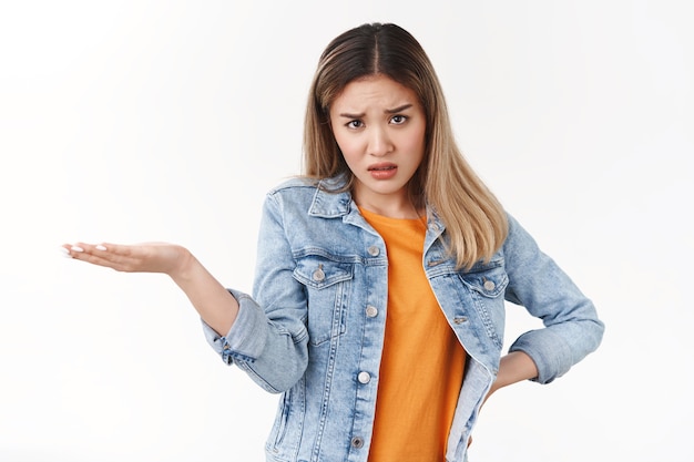 Angry intense displeased young bothered asian blond girl frowning frustrated hold confusing product hand look under forehead, complaining stare questioned