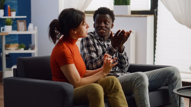 Angry interracial couple fighting on living room sofa