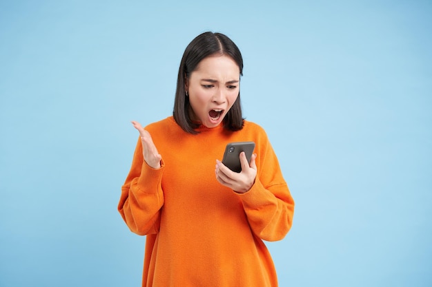 Free photo angry korean girl swearing and shouting at mobile phone looks outraged furious while reading news on