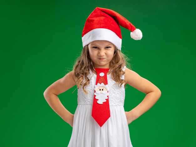 녹색 벽에 고립 된 엉덩이에 손을 댔을 넥타이와 크리스마스 모자를 쓰고 화가 어린 소녀