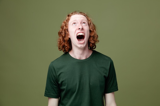 Angry looking at up young handsome guy wearing green t shirt isolated on green background