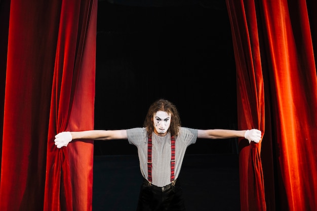 Angry male mime artist holding red curtain