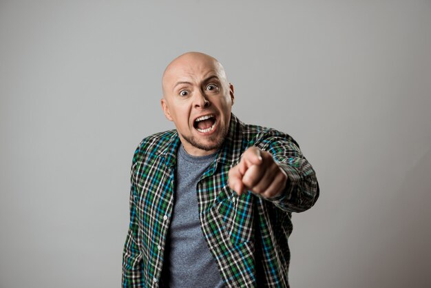 Angry man shouting, pointing finger over beige wall.