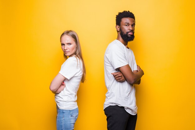 Angry man and woman being in fight and standing back to back with arms folded isolated over yellow wall