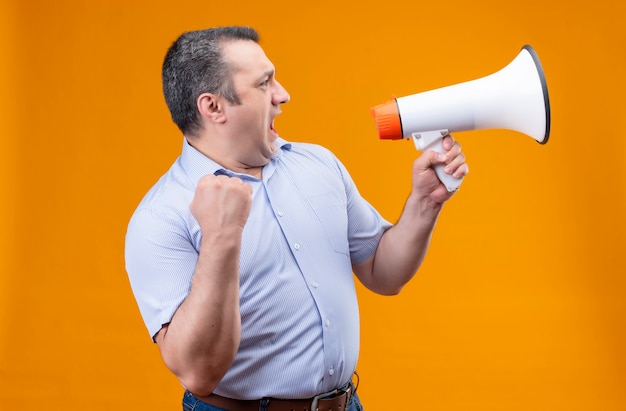 Angry middle age man in blue vertical striped shirt shouting on megaphone while standing