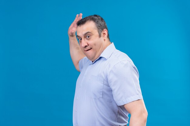 Angry middle-aged man in blue striped shirt raising his hand to slap on a blue space