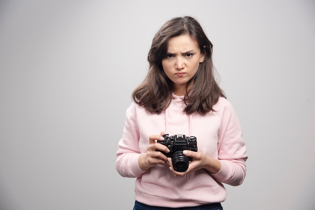 灰色の壁にカメラを保持している怒っている写真家。