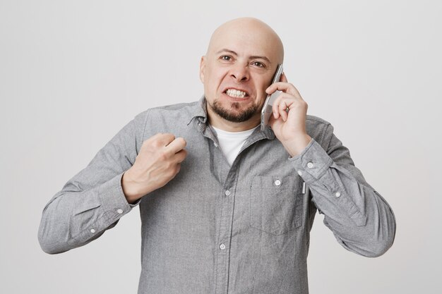 Angry pissed-off bald man clench fist, arguing on phone