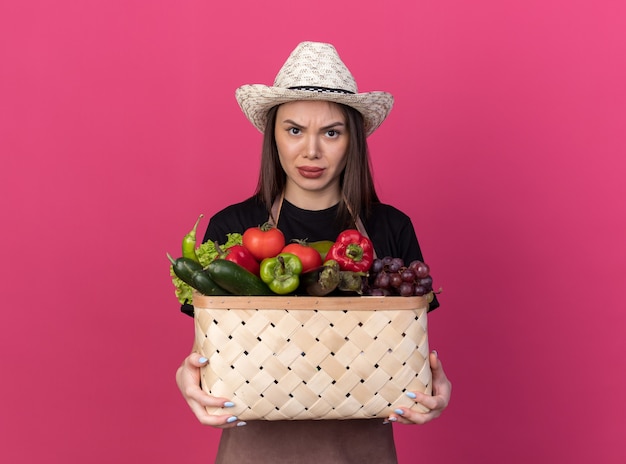 Giardiniere femmina caucasica piuttosto arrabbiato che indossa un cappello da giardinaggio che tiene cesto di verdure vegetable