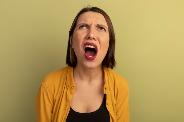 Angry pretty woman looks up isolated on olive green wall