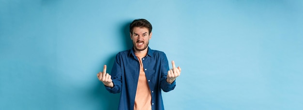 Free photo angry rude guy showing middle finger and saying fuck you swearing and staring furious at camera stan